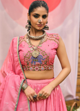 Woman in a traditional pink outfit with intricate designs and jewelry against a pink background